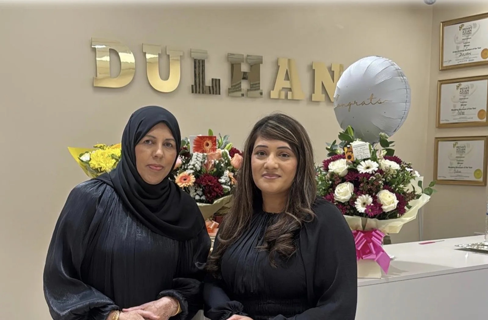 Dulhan founders Nazia and Zaibun standing together inside the boutique among flowers and the store awards
