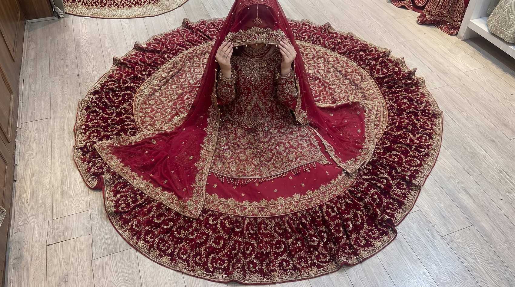 The heavily embroidered train of a red and gold bridal lehenga spread in a full circle on the floor, seen from above